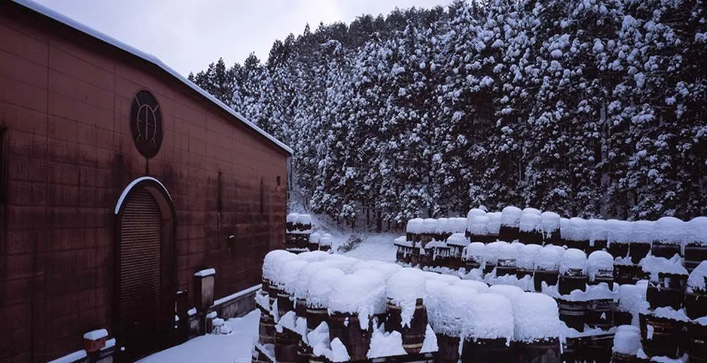 Casks stacked in front of Miyagikyo's red warehouse covered in snow in winter