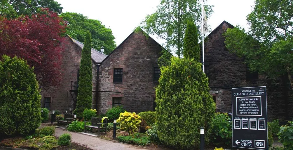 Glen Ord's visitor centre building made of stone hiding itself behind green trees and bushes