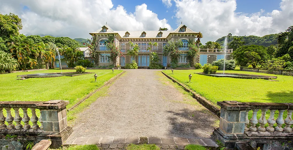 Entrance path to Depaz mansion between two green grass field with blue sky in the background