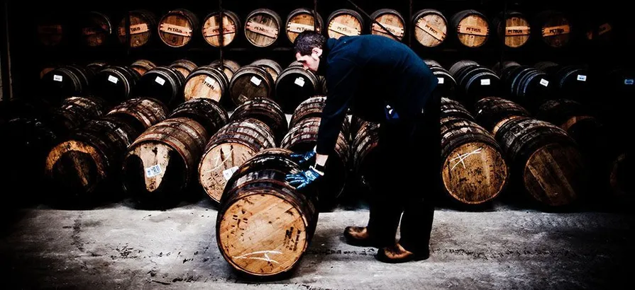 A worker at Bruichladdich distillery moving a cask in front of cask shelves
