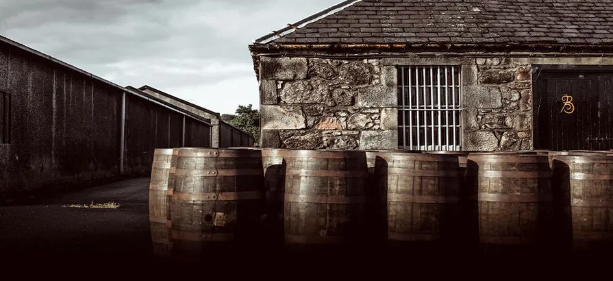 Casks standing in the front of Balblair's distillery building with grey sky in the back ground