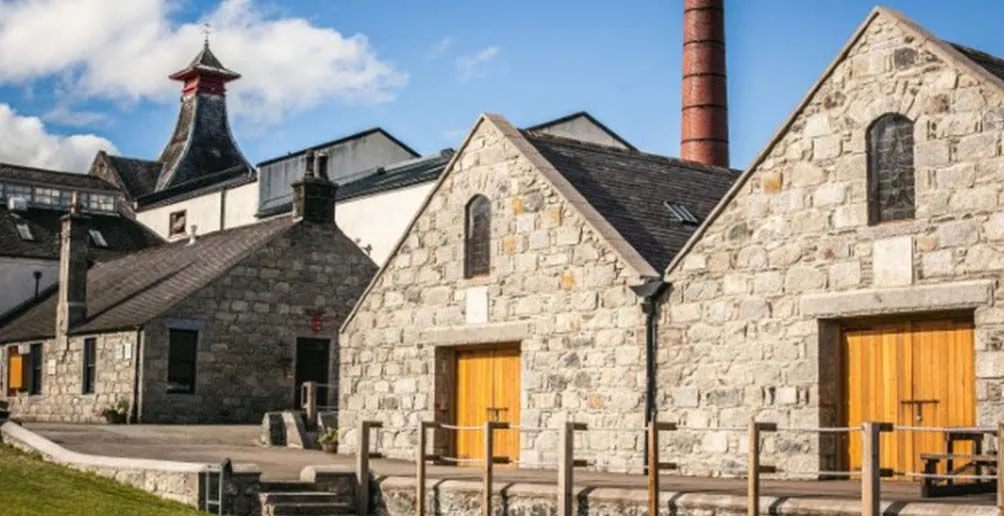 Stone buildings in Knockdu distillery with a red chimney located behind them and a pagoda style roof on the far left