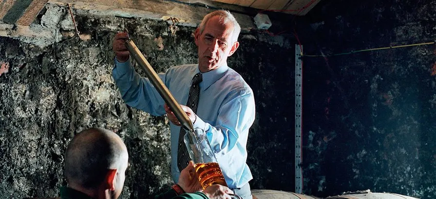 Master distiller taking a dram from a cask to check quality of the spirit